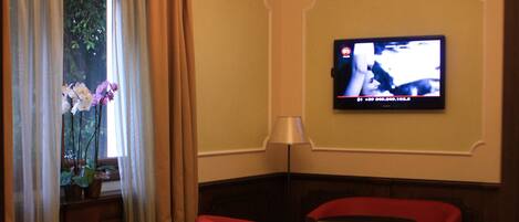 Ein Hotelzimmer mit Fernseher, roten Sesseln, einem Tisch und einer Kronleuchter.
