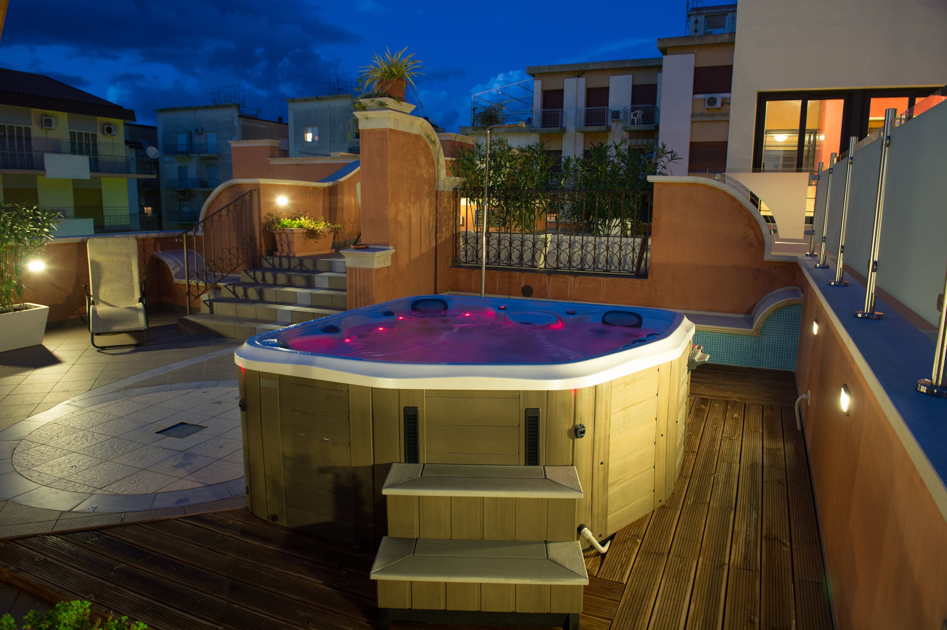A hot tub in a courtyard with steps leading up to it, surrounded by buildings and potted plants.