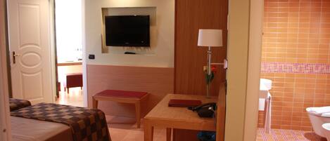 Una habitación de hotel con cama, escritorio, televisor y baño.