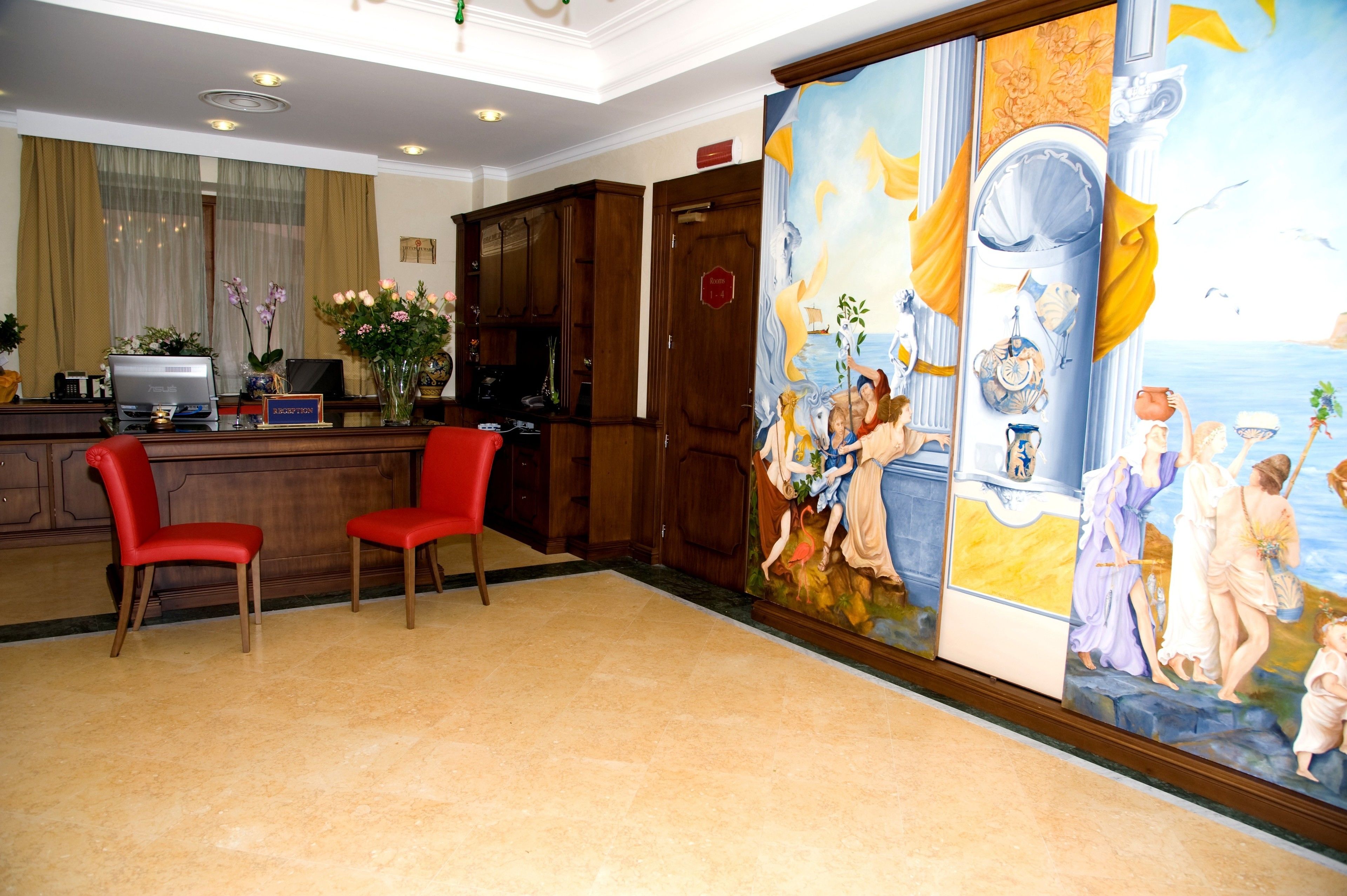 A lobby with a reception desk, two red chairs, a large mural, and wooden cabinets.