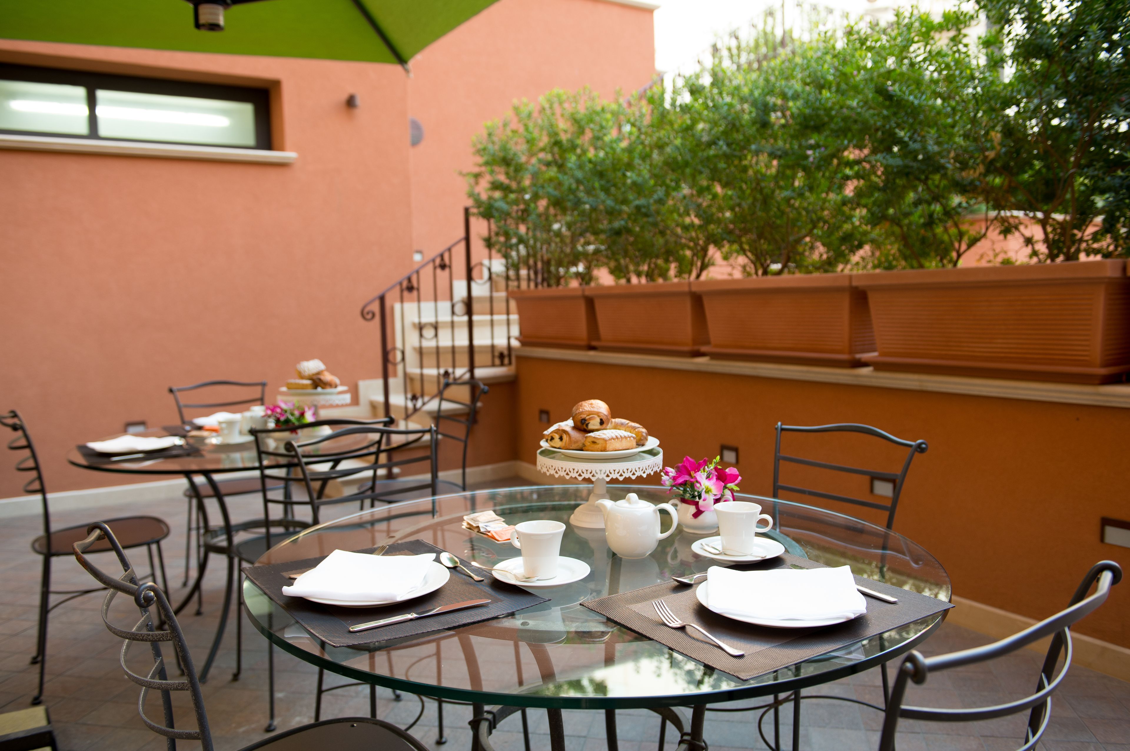 A glass table set for a meal with chairs, a cake stand, and a flower arrangement.