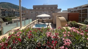 A rooftop terrace with a hot tub, outdoor seating, and a view of a residential area with a mountain in the background. - Artemis Hotel (Cefalù)