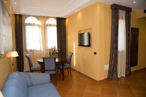 Habitación de hotel con sofá, una mesa de comedor con sillas, televisor de pantalla plana en la pared y cortinas en las ventanas.