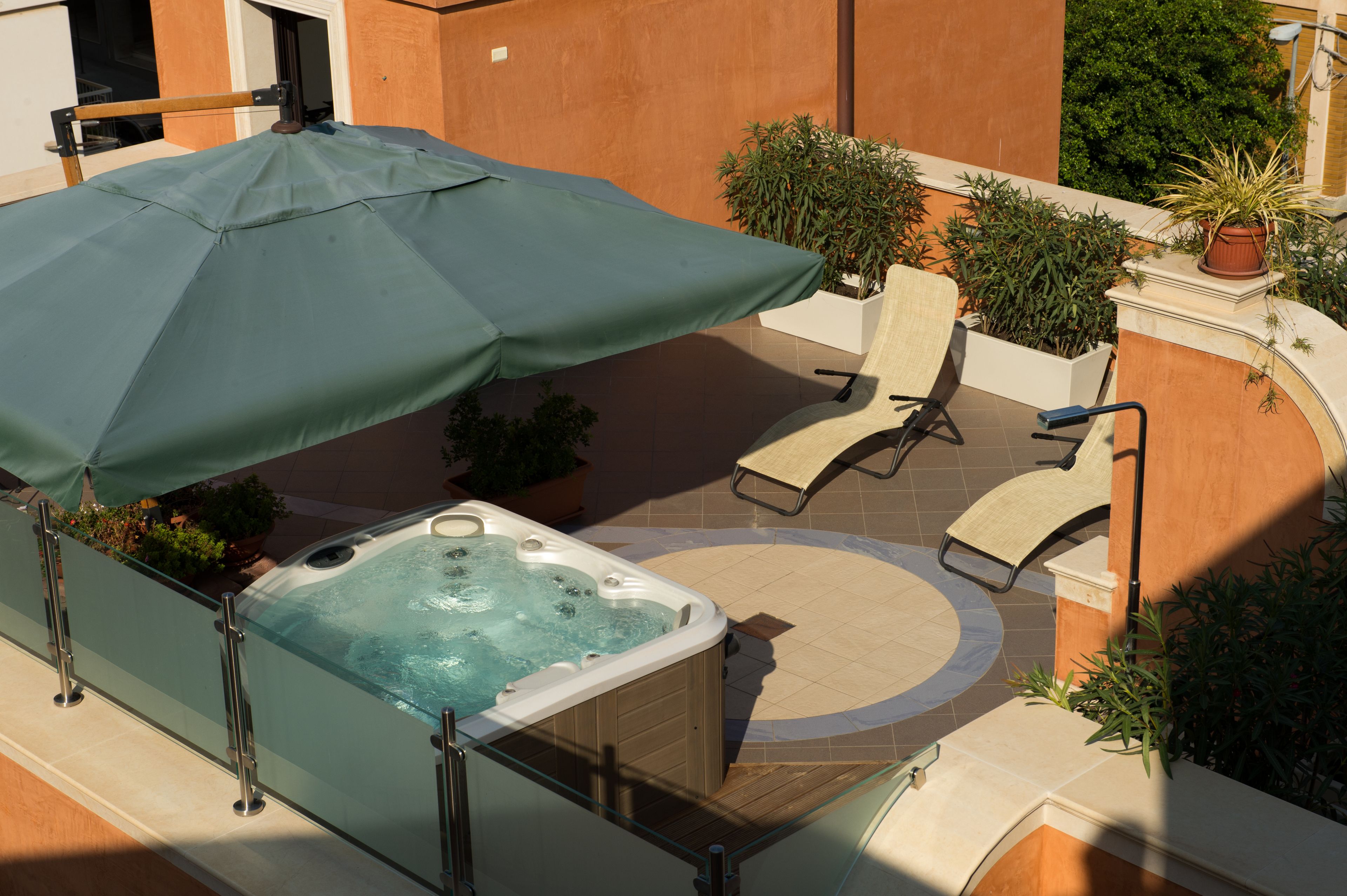 Un bain à remous avec un parasol, une chaise longue et des plantes en pot dans un espace extérieur.