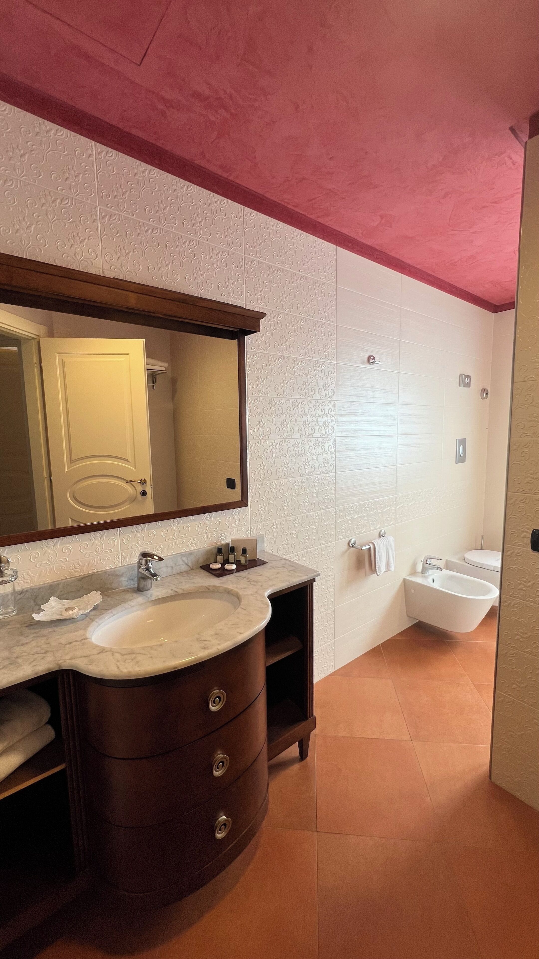 Un baño con lavamanos de mármol, un espejo grande, un mueble de tocador de madera, un bidé y una ducha.