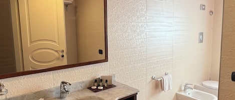 Un baño con lavamanos de mármol, un espejo grande, un mueble de tocador de madera, un bidé y una ducha.