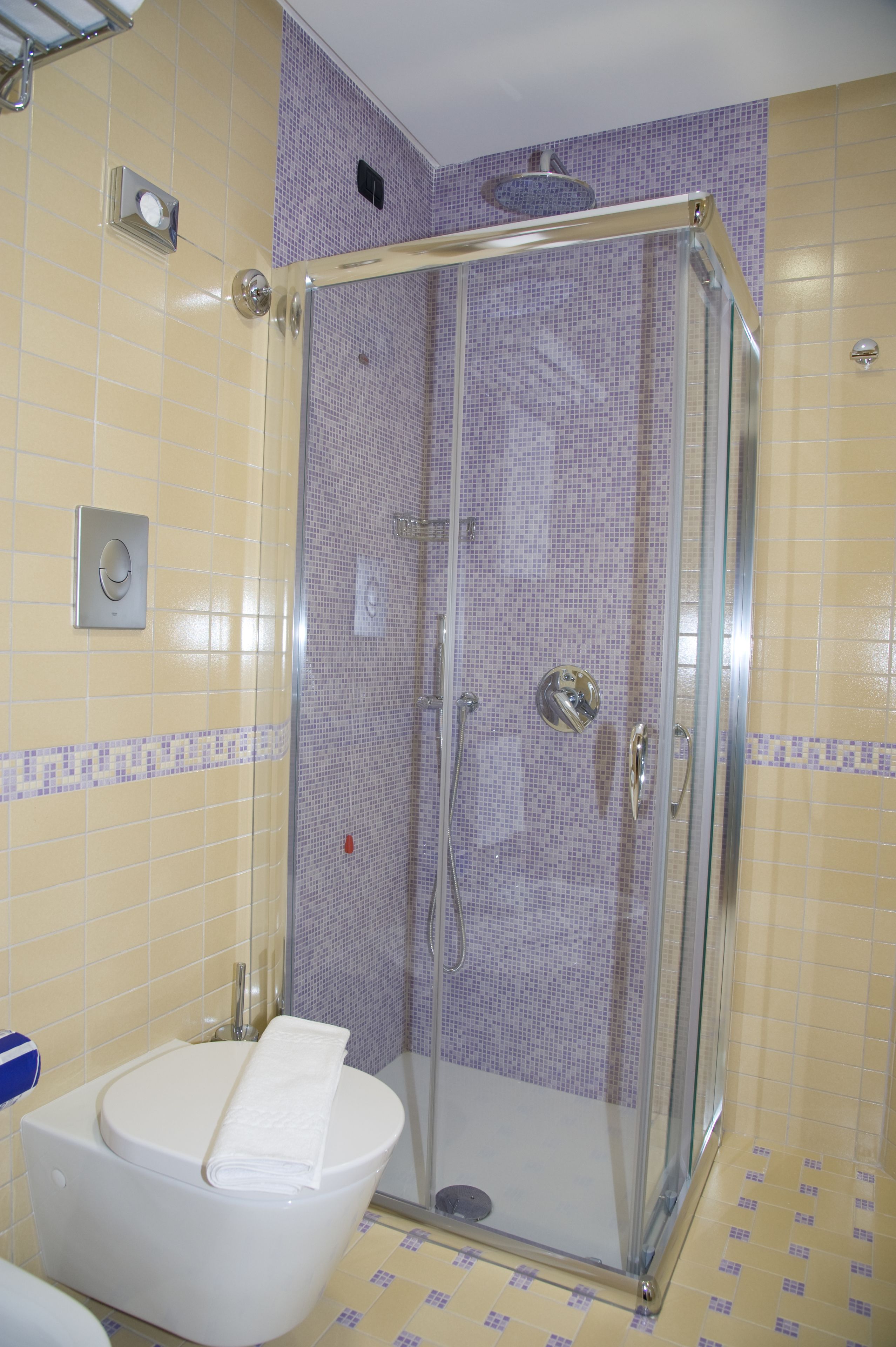 Un bagno con cabina doccia in vetro, un water con un asciugamano e pareti piastrellate.