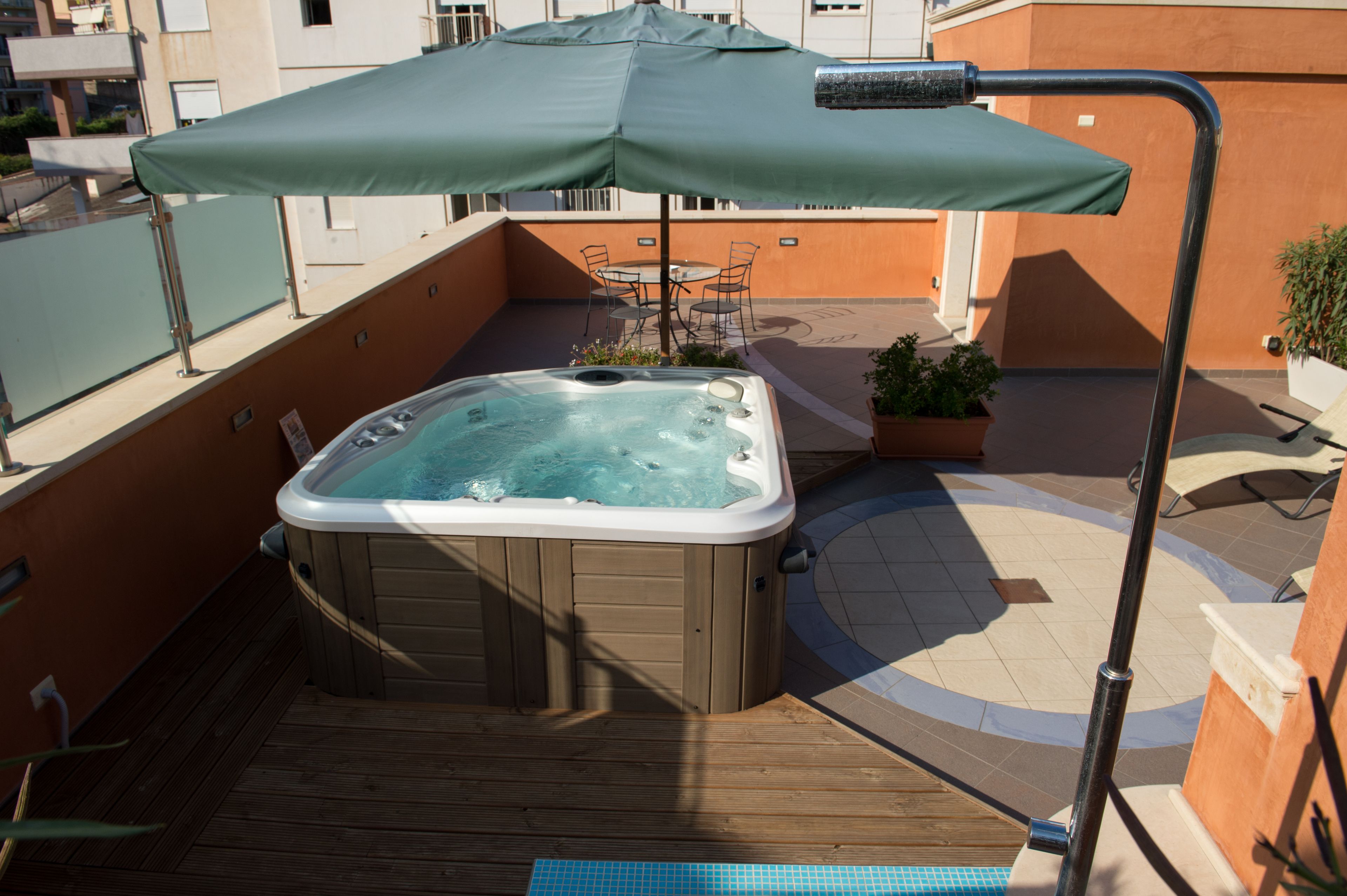Uma banheira de hidromassagem com guarda-sol verde, rodeada por um deck de madeira e uma piscina.
