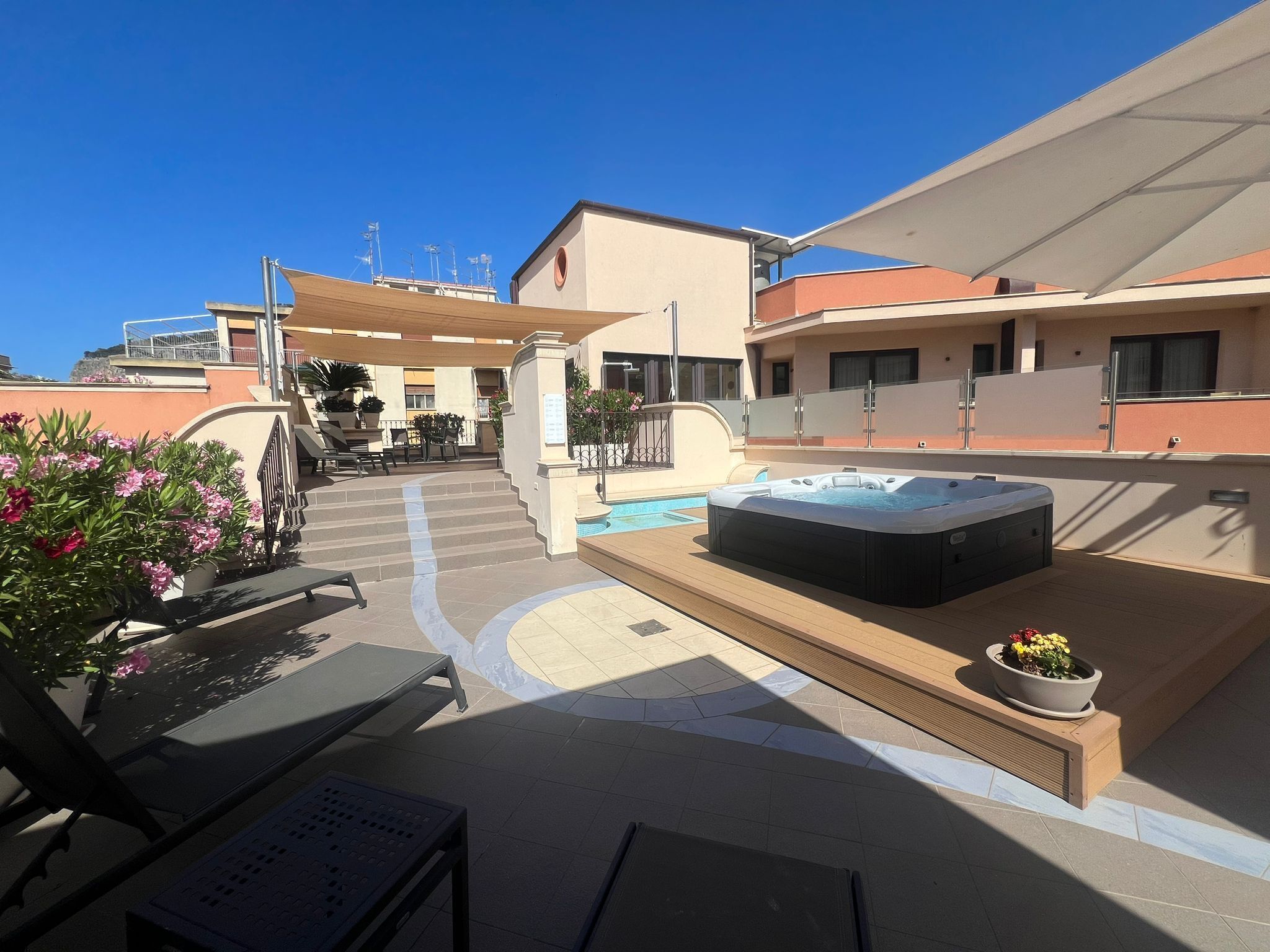 Een terras op het dak met een hottub, lounge stoelen en een zwembad.