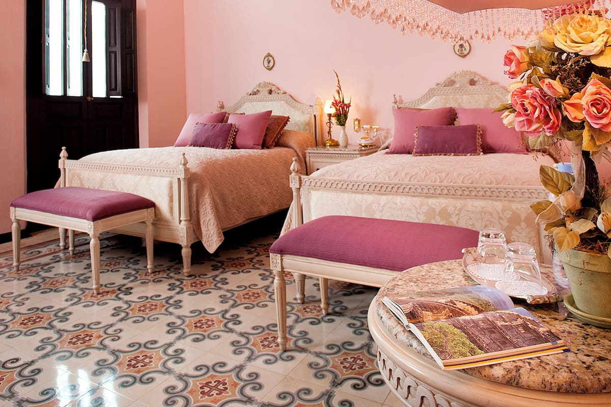 A bedroom with two beds, a chandelier, a decorative mirror, and a floral arrangement.