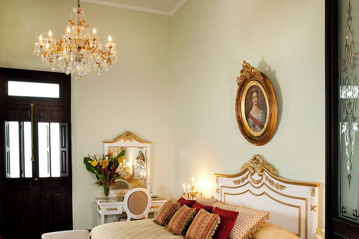 A bedroom with a large bed, a chandelier, a mirror, a dresser, and a door.