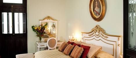 A bedroom with a large bed, a chandelier, a mirror, a dresser, and a door.