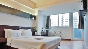 A hotel room with a large bed, a desk, and a chair. There is a window with curtains, a TV mounted on the wall, and a view of buildings outside. - Vela Boutique Hotel (Hong Kong)