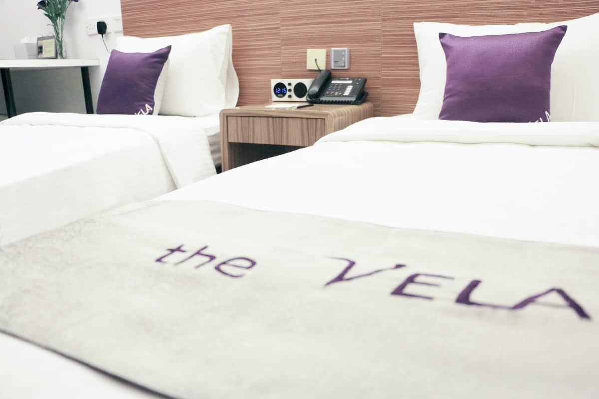 Ein Hotelzimmer mit zwei Betten, einem Nachttisch mit einem Radio und einem Kissen mit dem Schriftzug 'the VELA'.