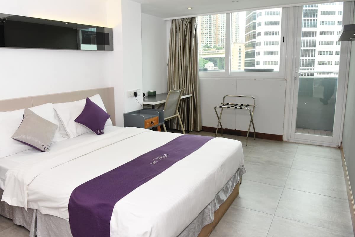 Ein Hotelzimmer mit Bett, Schreibtisch, Stuhl, einem Fenster mit Vorhängen und Blick auf Gebäude.