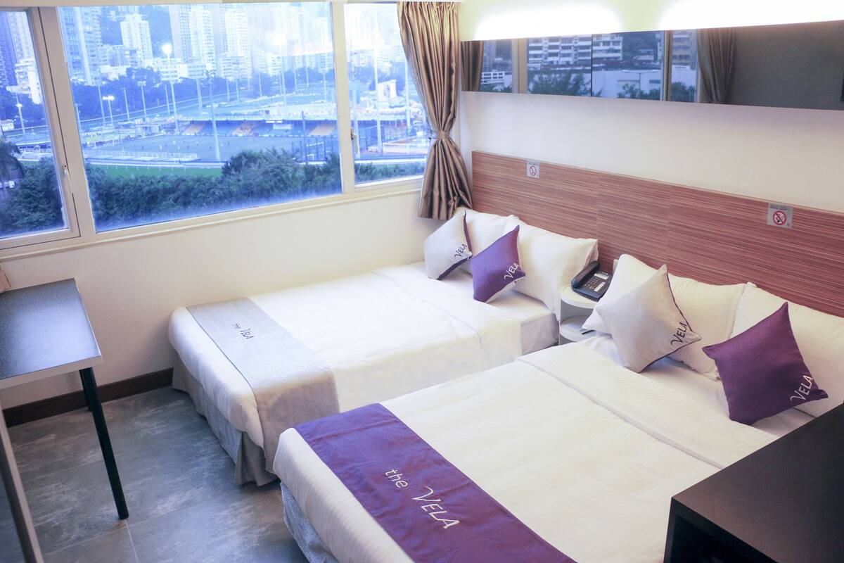 Ein Hotelzimmer mit zwei Betten, einem Schreibtisch und einem großen Fenster mit Blick auf die Stadt.