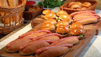 Una mesa de madera con salchichas, panes y canastas de pan, además de un plato de verduras.