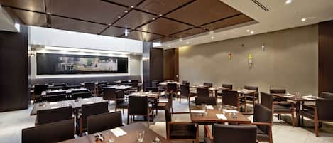 A conference room with multiple tables and chairs, a large screen, and a modern ceiling design.