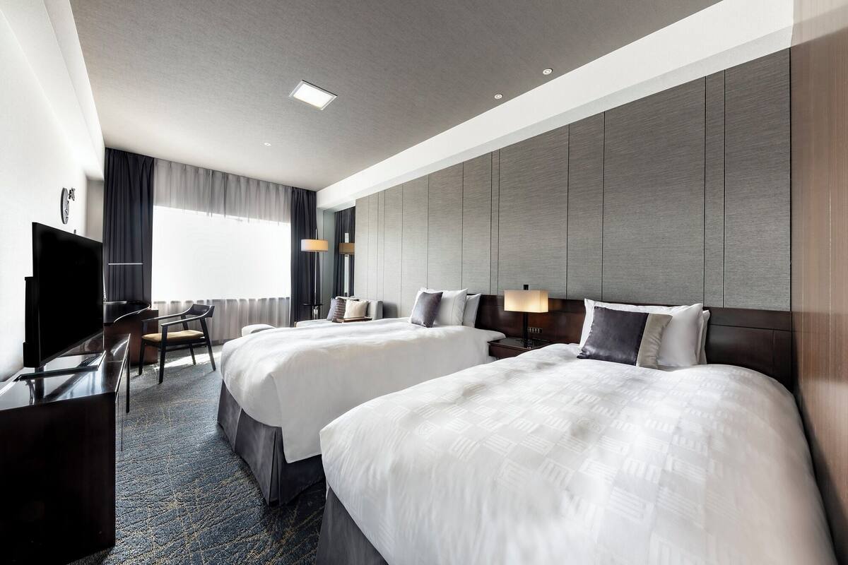 A hotel room with two beds, a TV, a desk, and a chair.