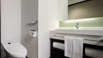 A modern bathroom with a toilet, a paper towel dispenser, a towel rack, and a sink with a mirror above it.