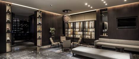 A modern lobby with marble flooring, a seating area with sofas and chairs, and a decorative wall with shelves.