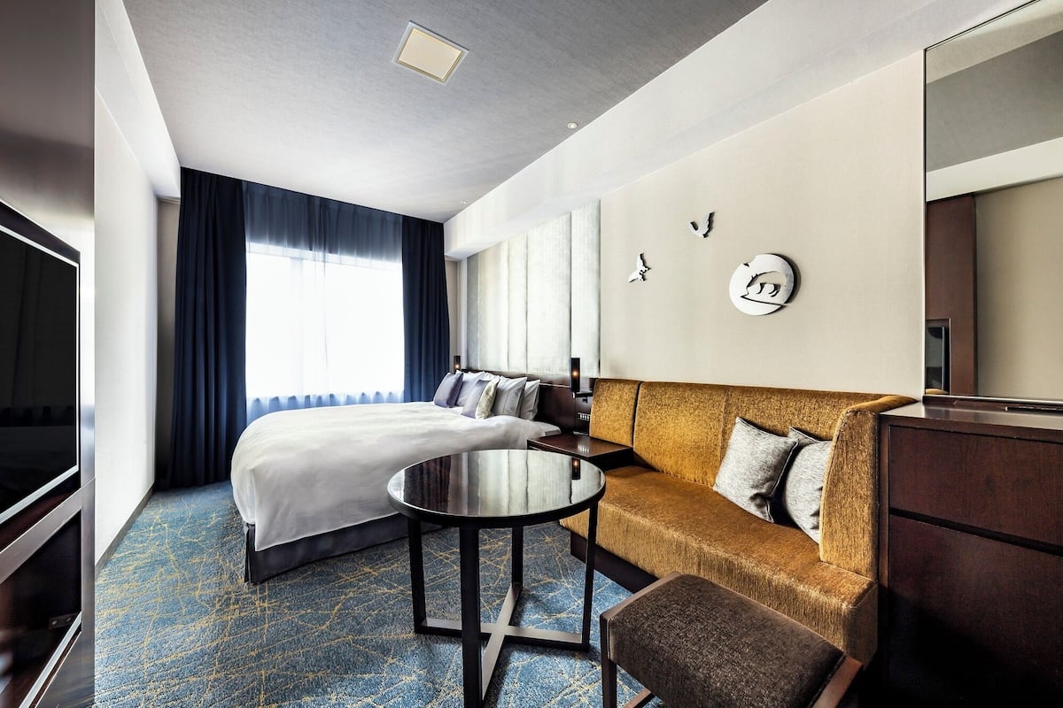 A hotel room with a bed, a sofa, a small table, and a mirror.