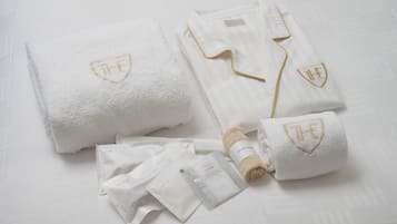 A neatly arranged set of white towels with embroidered logos, a folded shirt, and toiletries on a white surface.