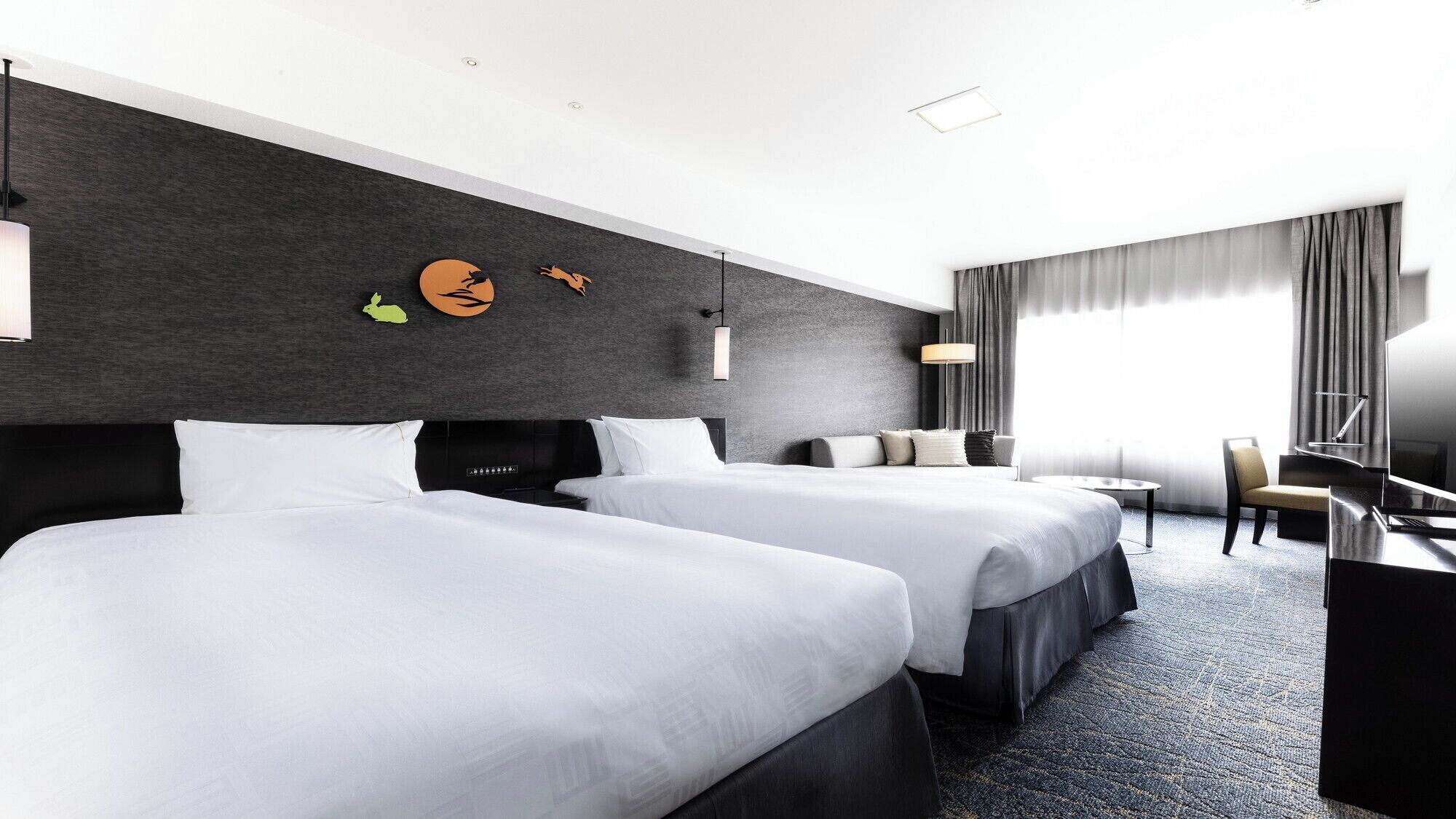 Habitación de hotel con dos camas, un escritorio, una silla, un televisor y un ventanal con cortinas.