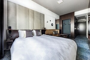 Una habitación de hotel moderna con una cama grande, un área de descanso, un armario y un baño visible a través de una puerta abierta.