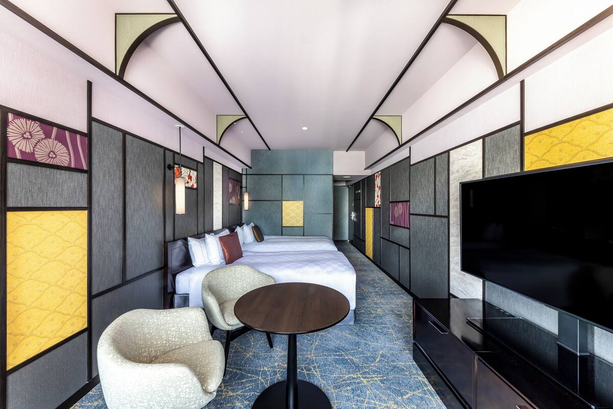 A hotel room with a large bed, a TV, a round table, and a seating area.
