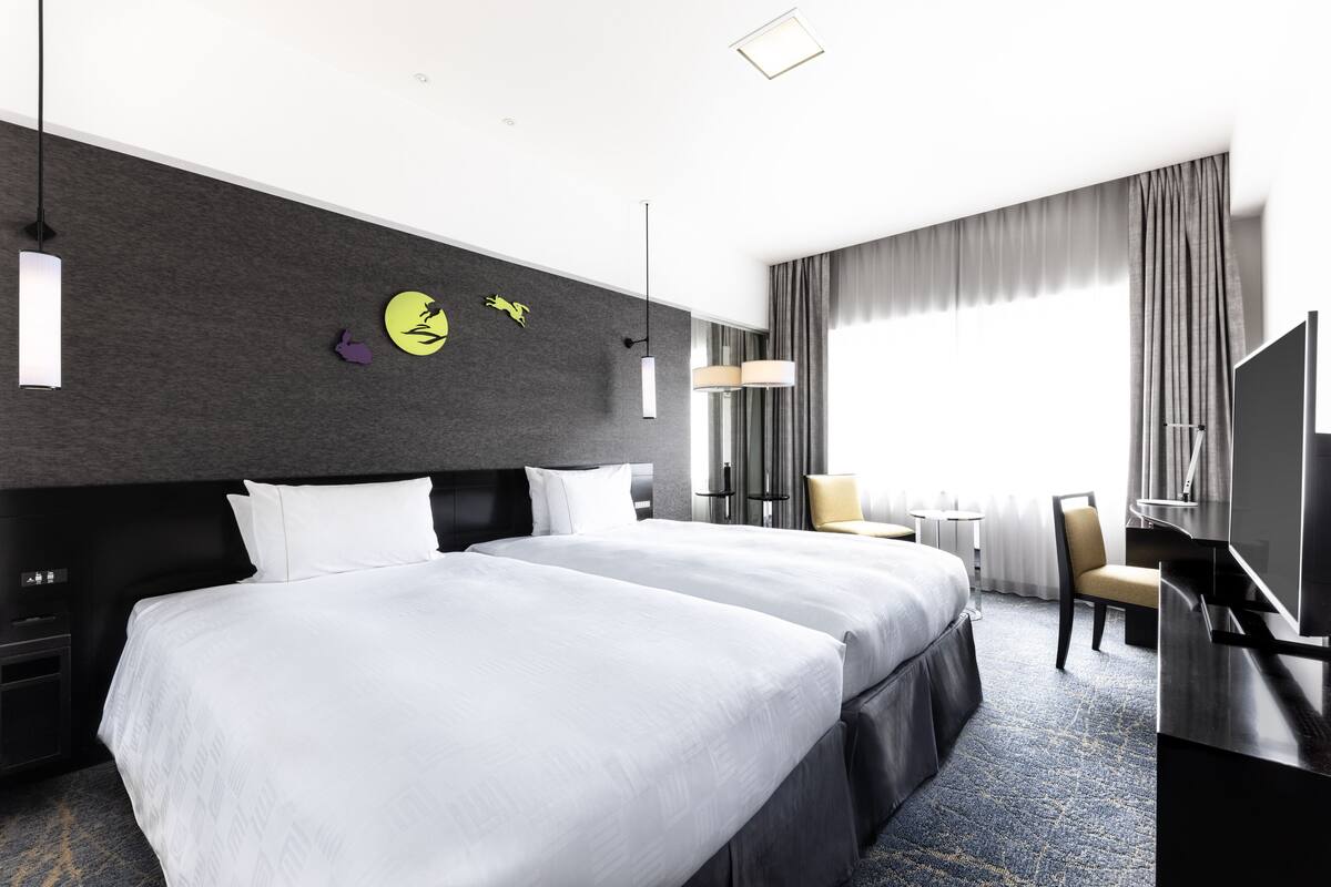 A modern hotel room with a large bed, a desk, a TV, and a view of the outdoors.