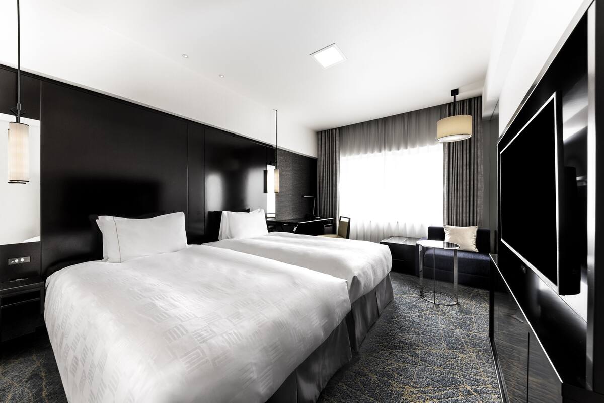A modern hotel room with a large bed, a desk, a TV, and a seating area.