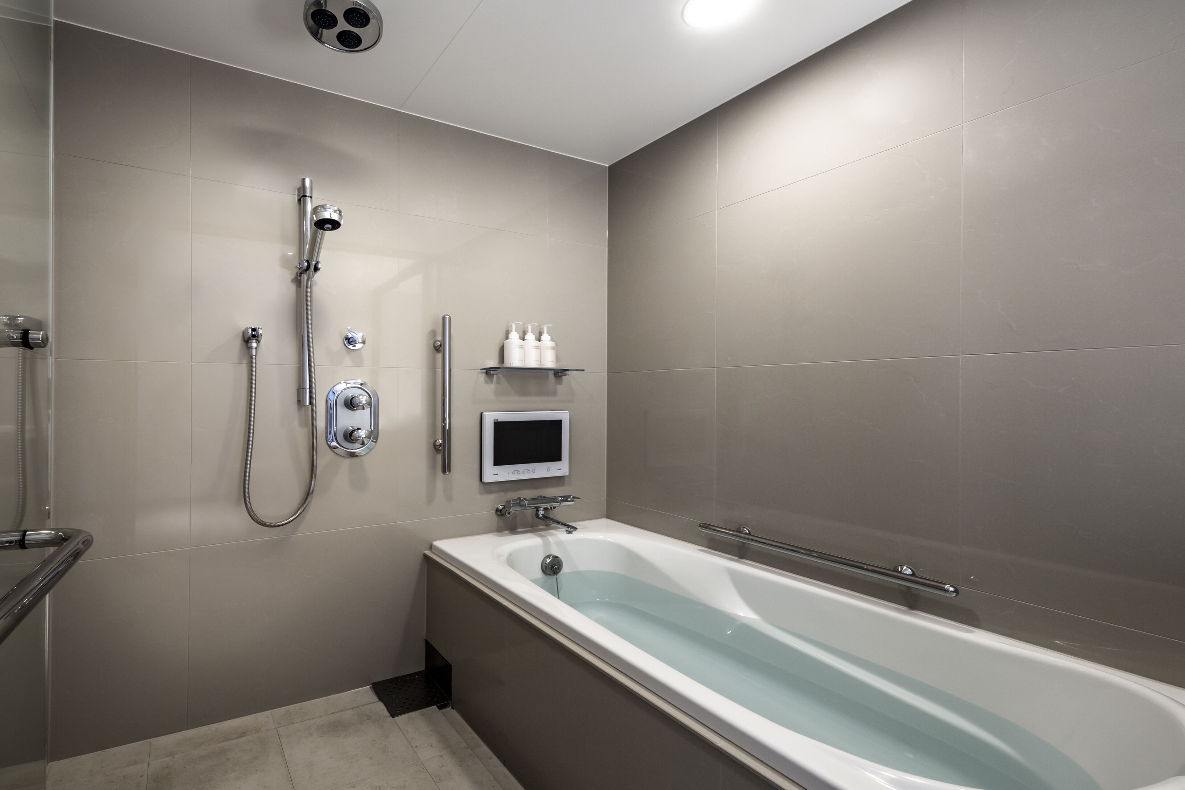 A modern bathroom with a bathtub, a handheld showerhead, and a wall-mounted control panel.