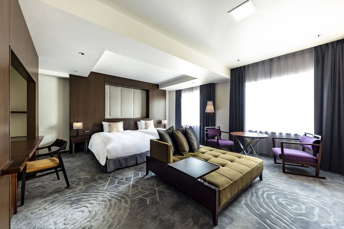 A hotel room with a bed, a sofa, a desk, and a chair.