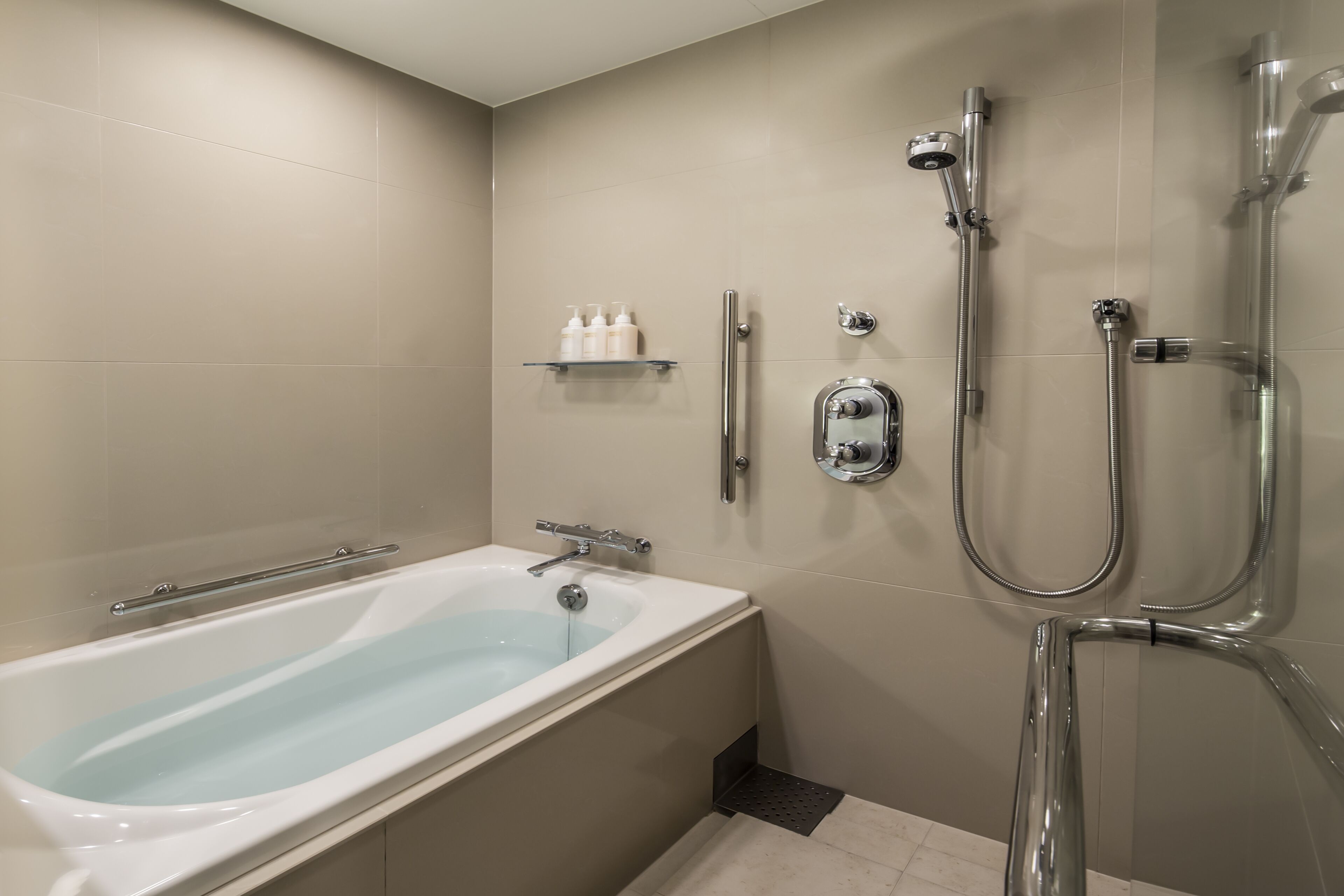 A modern bathroom with a bathtub, a shower with a handheld showerhead, and a glass shelf with toiletries.