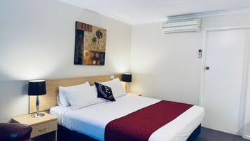 Een hotelkamer met een bed, nachtlampjes, een nachtkastje, een rode plaid, een wandairconditioner en een deur.