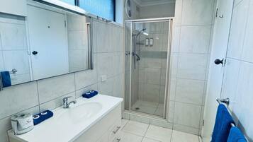 Un baño moderno con cabina de ducha de vidrio, un lavabo blanco y un espejo grande.