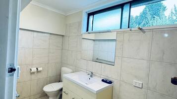 A bathroom with a toilet, sink, cabinet, and a window with a view of trees.