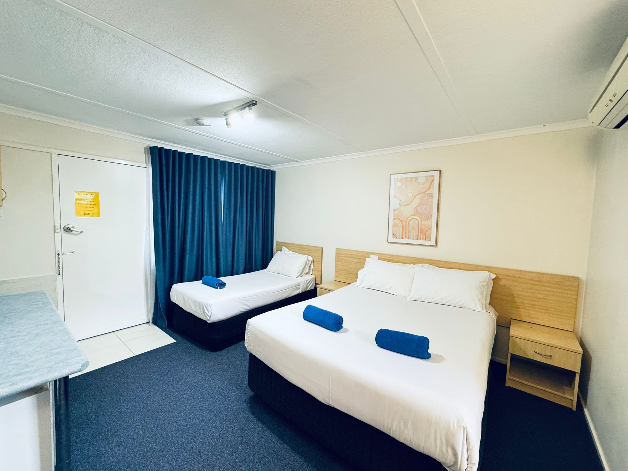 Een hotelkamer met twee bedden, een bureau, een stoel, een kledingkast en een schilderij aan de muur.