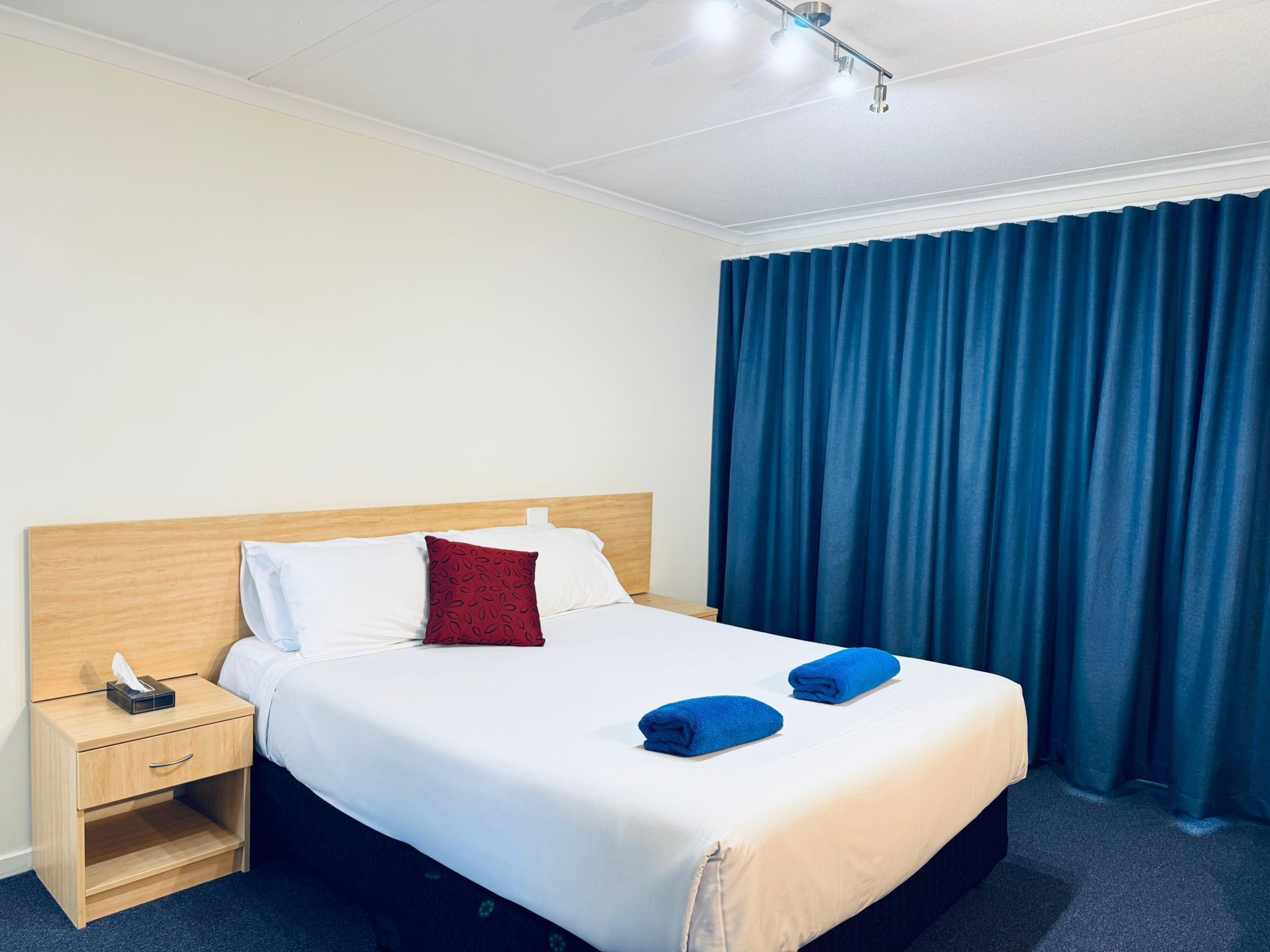 Una habitación de hotel con cama, mesita de noche, lámpara y ventana con cortinas.