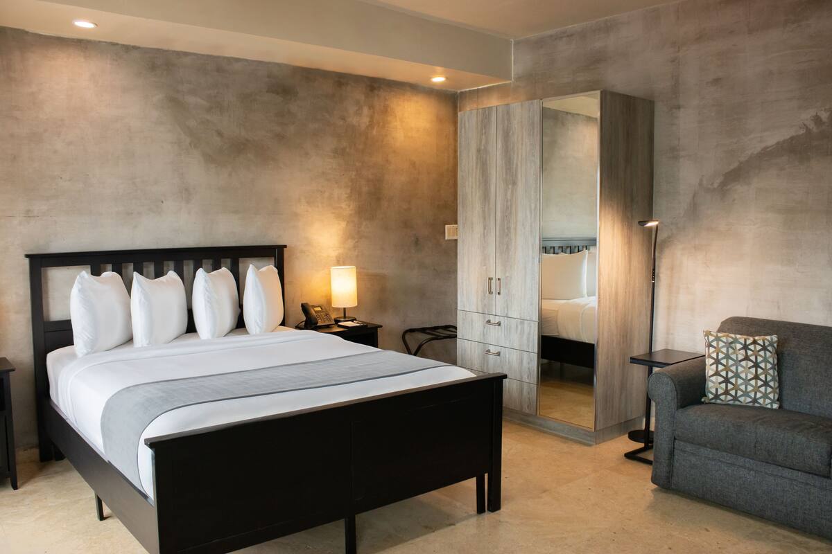 Un dormitorio con cama, mesita de noche, lámpara, armario y un sofá.