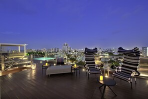 A rooftop terrace with a pool, seating area, and city views at dusk. -  Ciqala Suites Hotel (San Juan)
