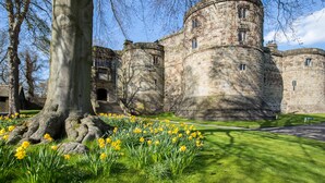 A historic stone castle with round towers, surrounded by a well-maintained lawn and vibrant yellow daffodils. - The Coniston Hotel (Skipton)
