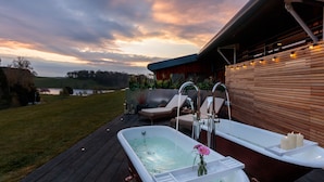 A spa area with a hot tub, lounge chairs, and a view of a lake at sunset. - The Coniston Hotel and Country Estate (Skipton)