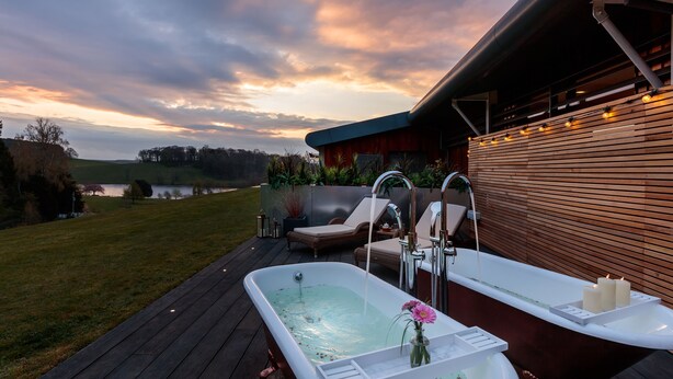 A spa area with a hot tub, lounge chairs, and a view of a lake at sunset. - The Coniston Hotel (Skipton)