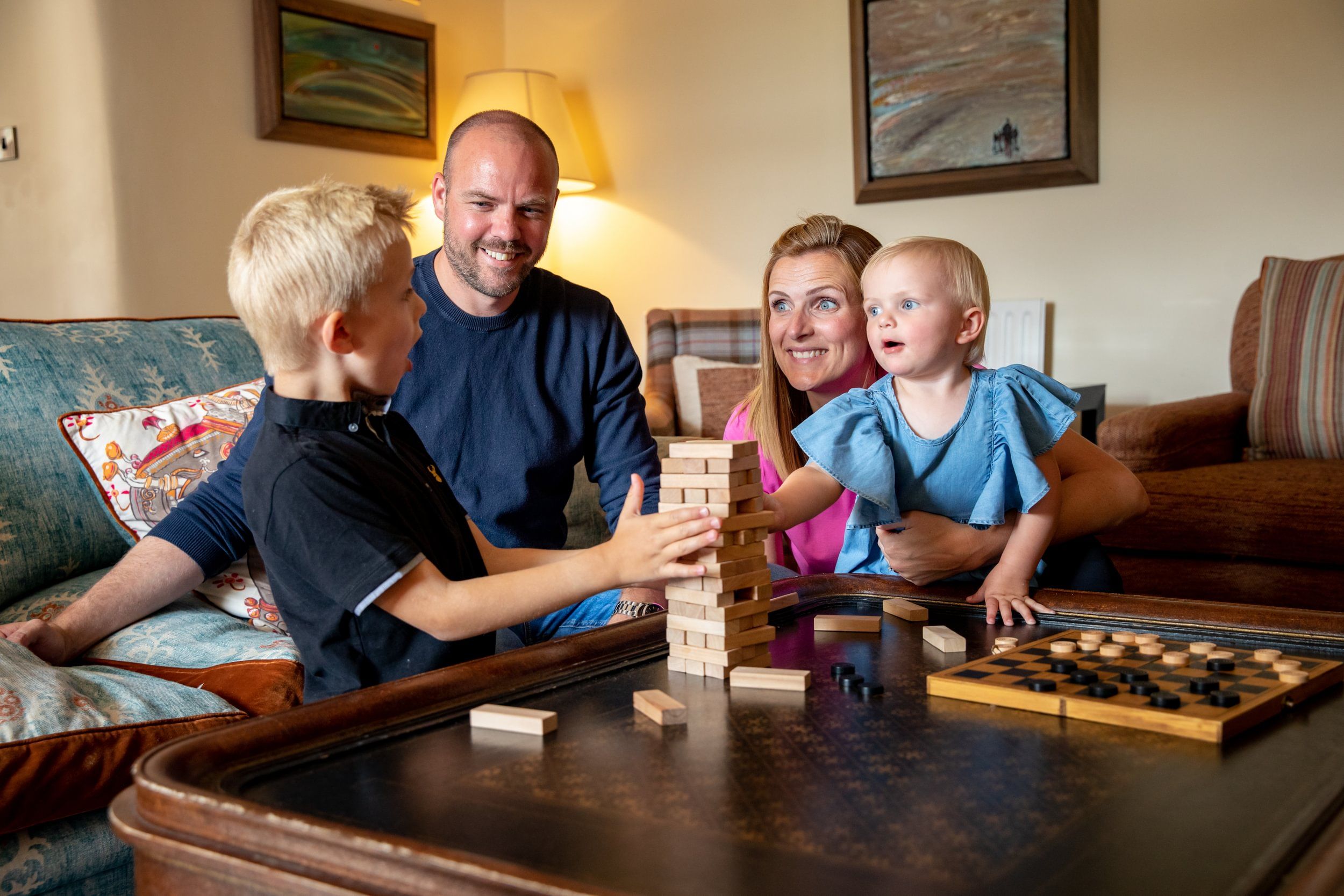 Una familia jugando un juego de mesa en una mesa de madera en una sala de estar con un sofá y cojines.