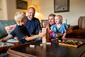 A family playing a board game at a wooden table in a living room with a sofa and cushions. - The Coniston Hotel (Skipton)