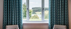 A room with a window overlooking a landscape, curtains with a geometric pattern, and two patterned cushions. - The Coniston Hotel (Skipton)