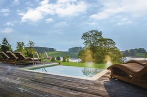 A wooden deck with a swimming pool, lounge chairs, and a view of a lake and hills. - The Coniston Hotel (Skipton)