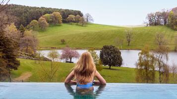 Guests can enjoy serene views of lush green landscapes and a body of water from the poolside.